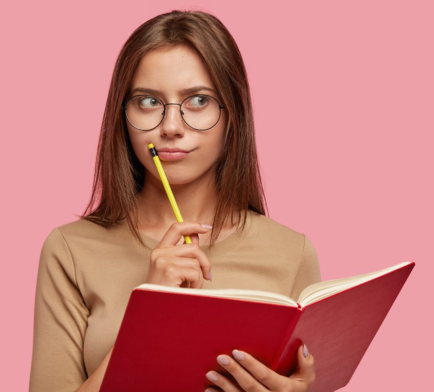 Pensive female writer ponders new ideas holds red notebook pencil near mouth has thoughtful expression cropped